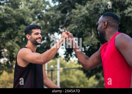 Junge männliche Freunde spielen Basketball in Sportbekleidung auf einem Stadtplatz in der Stadt. Sie haben Spaß und High Five, die den Sport genießen. Stockfoto