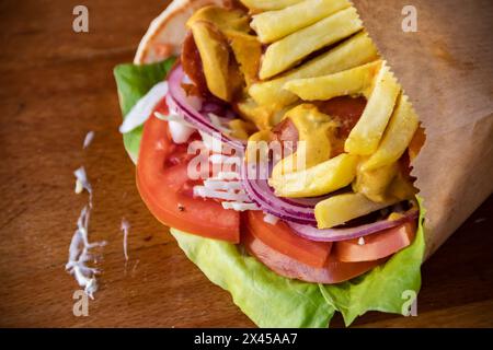 Aromatisches Tortilla-Wrap mit herzhaften Würstchen, Pommes frites, grünem Salat, Tomaten, Zwiebeln, und Kohl, alles verpackt für unterwegs Stockfoto