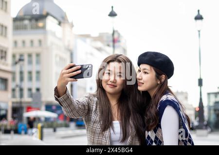 Zwei junge asiatische Freundinnen laufen auf der Straße von Madrid und machen Selfies mit dem Smartphone Stockfoto
