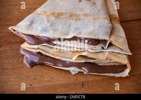 Haufen hausgemachter Pfannkuchen gefüllt mit tropfender geschmolzener heißer Schokolade, Schokolade tropft auf dem Tisch aus den Pfannkuchen Stockfoto