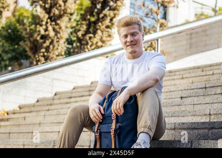 Albino latin Mann in weißen Kleidern, sitzt auf einer Treppe auf der Straße, blickt auf die Kamera und lächelt Stockfoto