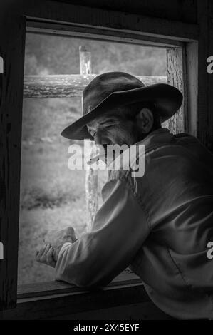 Ein Tabakbauer mit Cowboyhut raucht eine Zigarre am Fenster seines Bauernhauses im Vinales Valley, Vinales, Kuba. Stockfoto