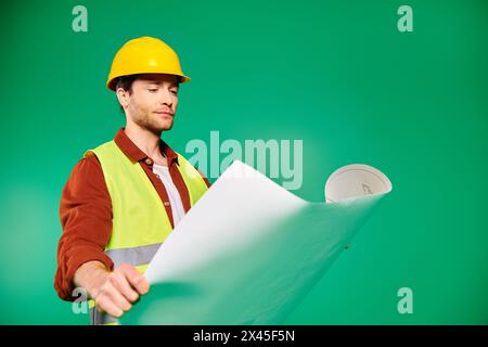 Ein gutaussehender Mann mit einem Schutzhelm hält einen Plan selbstbewusst. Stockfoto