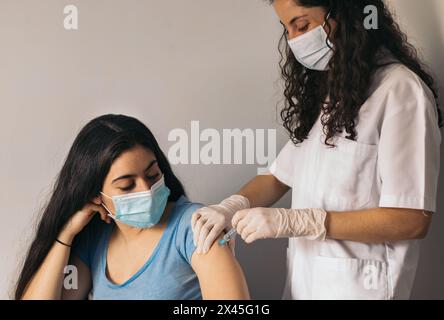 Arzt macht Impfung für junge Frau mit chirurgischer Maske Stockfoto