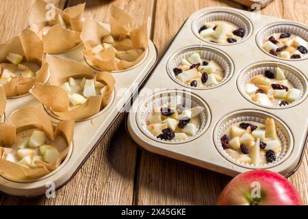 Beim Kochen werden hausgemachte Muffins mit Äpfeln und Rosinen zubereitet. Auf einem Holztisch Stockfoto