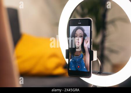 Junge Influencerin, die einen Make-up-Video-Blog für soziale Medien macht. Sie wird mit einem Smartphone und mit einem Leuchtring zu Hause aufgenommen. Schönheitsbegriff Stockfoto