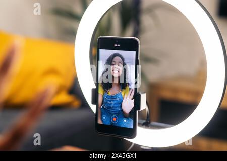 Inhalte erstellen: Junge Frau nimmt sich mit Smartphone und Ringlicht auf dem Sofa auf Stockfoto