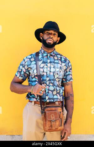 Porträt eines stilvollen schwarzen Mannes mit Hut und alternativem Outfit auf gelbem Hintergrund Stockfoto
