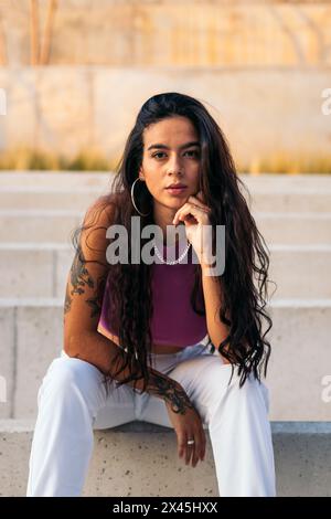 Porträt einer jungen Latina-Frau mit Tattoos und Piercings, die auf einigen Stufen in der Stadt sitzt und auf die Kamera blickt Stockfoto