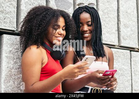 Zwei afroamerikanische Mädchen mit Afro-Haaren laufen in einem Park und lachen mit einem Smartphone Stockfoto