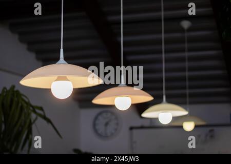 Eine Reihe eleganter Lampen mit Metallschirmen hängt von der Decke, die Schatten und Lichttöne hervorbringen. Eine Uhr im Hintergrund trägt zur Atmosphäre bei Stockfoto