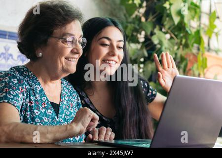 Lächelnde ältere Frau, die zu Hause einen Laptop benutzt und mit ihrer Enkelin einen Videoanruf führt. Die beiden lächeln und freuen sich, die gemeinsame Zeit zu genießen Stockfoto