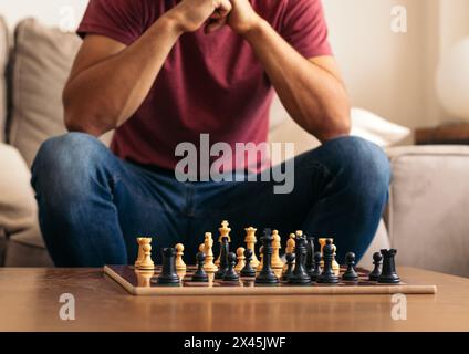 Das Schachspiel beginnt gleich. Nicht erkennbarer Mann, der auf einem Sofa vor einem Schachbrett sitzt, mit den Stücken. Stockfoto
