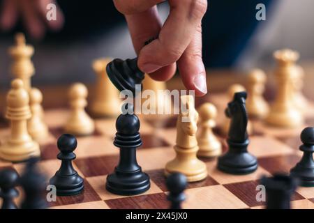 Unerkennbare Hand eines Mannes, der Schach spielt. Er nimmt eines der schwarzen Stücke, um den weißen Ritter seines Gegners zu fressen Stockfoto