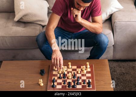 Schachspiel zwischen Freunden. Junger Mann, der auf dem Sofa im Wohnzimmer sitzt und zu Hause Schach spielt. Hoher Winkel der Platine mit weiß und Schwarz Stockfoto