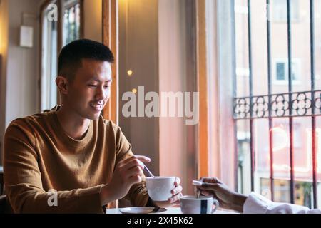 Nahaufnahme eines lächelnden asiatischen Mannes, der Kaffee in einem Café mit unbekannter Frau trinkt Stockfoto