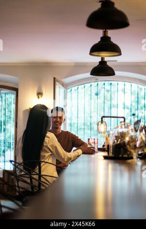 Lateinamerikanische Frau und asiatischer Mann, die einen Cocktail an einer Bar trinken und sich amüsieren. Sie treffen sich zu einem ersten Date Stockfoto