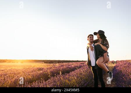 Ein junger Mann, der seine Freundin beim Gehen auf dem Feld mit dem Huckepack versorgt. Stockfoto