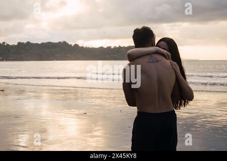 Romantisches Foto von einem Paar, das am Strand den Sonnenuntergang beobachtet Stockfoto