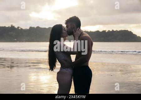 Ein junges Paar an einem wunderschönen Strand in Costa Rica, küsst sich und beobachtet den Sonnenuntergang Stockfoto