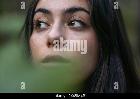 Nahporträt einer schönen jungen Frau im Wald, gesehen durch die Blätter von Pflanzen Stockfoto