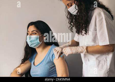Arzt macht Impfung für junge Frau mit chirurgischer Maske Stockfoto