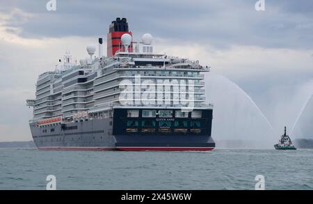 Ein Schlepper sprüht Wasser, als Cunards neuestes Kreuzfahrtschiff Queen Anne am City Cruise Terminal in Southampton, Hampshire, ankommt, nachdem sie nach fünf Jahren Bauzeit in Italien von der Werft Fincantieri Marghera in Venedig ausgelaufen ist. Das Kreuzfahrtschiff kann 3000 Gäste aufnehmen und wird nächsten Monat ihre Jungfernfahrt Unternehmen. Bilddatum: Dienstag, 30. April 2024. Stockfoto