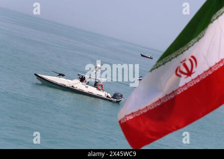 April 2024, Persischer Golf, Buschehr, Iran: die Schnellboote des Korps der Islamischen Revolutionsgarde (IRGC) segeln entlang des Persischen Golfs, während die iranische Flagge während der Marineparade der IRGC zum Nationalfeiertag des Persischen Golfs in der Nähe des Kernkraftwerks Bushehr in der Hafenstadt Bushehr in der Provinz Bushehr im Süden des Iran winkt. Der Iran feiert den Jahrestag der Befreiung des Südens des Landes von der portugiesischen Besatzung im Jahr 1622 als „Nationalfeiertag am Persischen Golf“ am 29. April 2024 in Buschehr. Das Datum fällt mit dem Jahrestag eines erfolgreichen Militärkampfes von Shah Abbas zusammen. Stockfoto