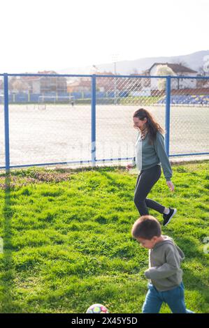 Mit einer wachsamen Ameise in der Nähe führt ein Kleinkind eine Jagd nach dem Fußball mit drei Jahren auf dem Rasenfeld Stockfoto