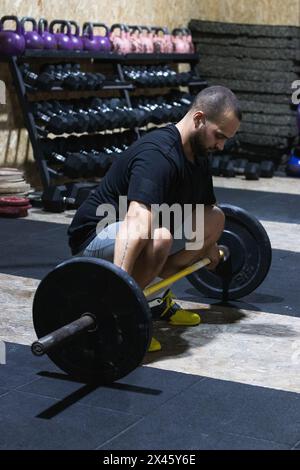 Ganzkörper eines fokussierten hispanischen bärtigen männlichen Athleten, der mit einer schweren Langhantel hockt, um beim Gewichtheben im Sportzentrum eine Entlastungsübung zu absolvieren Stockfoto