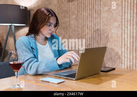 Junge Managerin in smarter Freizeitkleidung und Brille, die mit Stift auf den Netbook-Bildschirm zeigt und Daten analysiert, während sie an einem Remote-Projekt in Res arbeitet Stockfoto