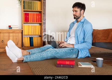 Junger Mann, der am Laptop arbeitet, während er auf Holzboden sitzt Stockfoto