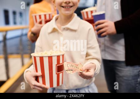 Das Mädchen hält fröhlich einen Eimer Popcorn und Tickets in einem Kino, umgeben von seiner glücklichen Familie. Stockfoto