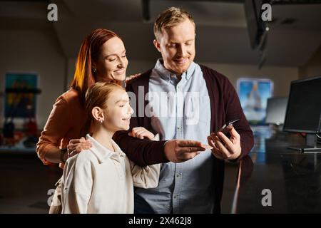 Ein Mann und eine Familie drängen sich glücklich zusammen, vertieft in den Bildschirm eines Mobiltelefons, das sie sehen. Stockfoto