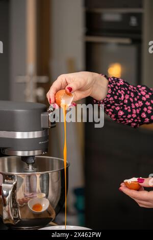 Ein Bäcker trennt ein Ei fachmännisch und lässt das goldene Eigelb in eine Rührschüssel fallen, die vor dem Hintergrund einer modernen Küche steht. Hochwertiges Foto Stockfoto