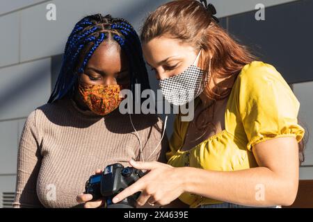 Begeisterte diverse Freundinnen, die Musik hören und durchschauen Fotos auf Fotokamera auf der Straße gemacht Stockfoto