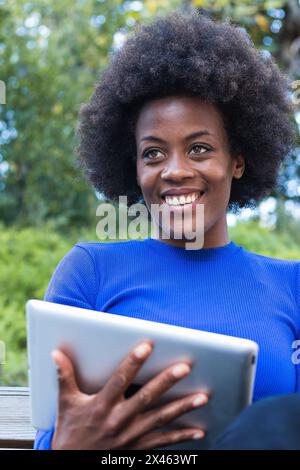 Inhalt Afrikanisch-amerikanische Freiberuflerin sitzt auf der Bank im Park Und mit Tablet arbeiten, während Remote auf Startup-Projekt Stockfoto