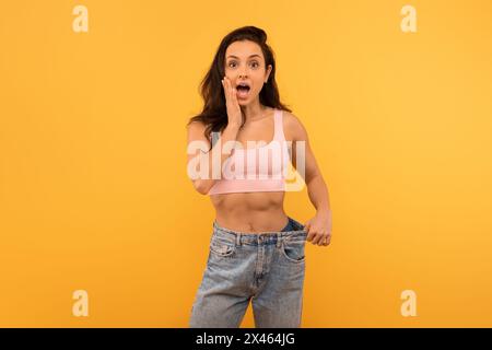 Überraschte junge Frau in rosafarbenem Crop Top und übergroßer Jeans Stockfoto