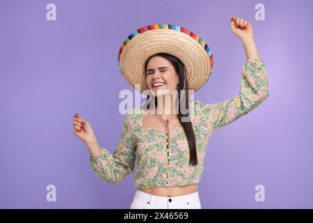 Junge Frau mit mexikanischem Sombrero-Hut, der auf violettem Hintergrund tanzt Stockfoto