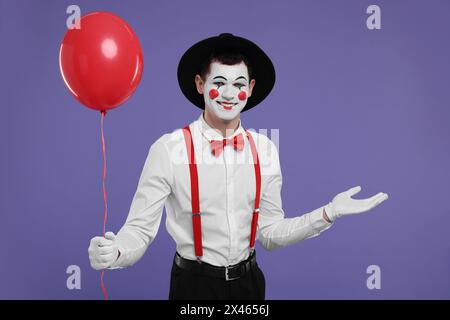 Lustiger Mime-Künstler mit rotem Ballon auf violettem Hintergrund Stockfoto