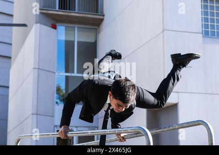 Männlicher Unternehmer in edlem Anzug Balancing in Handstand auf Metall Geländer in der Stadt, während vorformende Parkour Trick Stockfoto