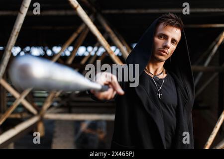 Ernster Mann in schwarzer Kleidung mit Kapuze hält Eine Fledermaus. Stockfoto