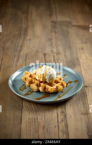 Teller mit belgischen Waffeln, dekoriert mit Karamellsauce und Vanilleeis auf Holztisch Stockfoto