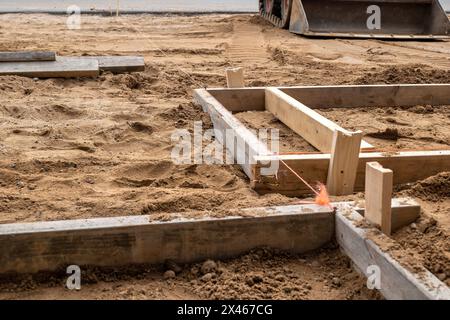 Eine Holzform zur Zementplatzierung im braunen Schmutz auf einer Baustelle. Zwei mal vier Bretter, Schnur, Schmutz und ein Frontlader. Stockfoto