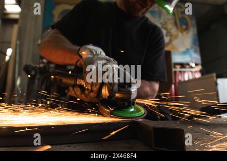 Von unten abgeschnitten unkenntlich männlichen Schweißer in Schutzhardhat mit Elektrische Mühle und Schneiden Metall Detail in grungy Werkstatt Stockfoto