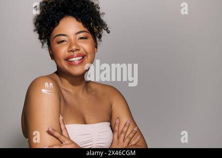 Eine schöne junge afroamerikanische Frau mit lockigen Haaren posiert selbstbewusst und kreuzt ihre Arme für ein Porträt in einem Studio-Setting. Stockfoto