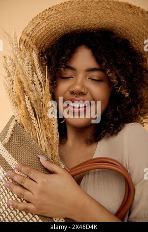 Schöne afroamerikanische Frau mit lockigen Haaren, mit Strohhut und Handtasche in einem Studio-Setting. Stockfoto