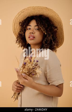 Eine schöne junge afroamerikanische Frau mit lockigem Haar, mit Strohhut und Blumen in einem Studio. Stockfoto