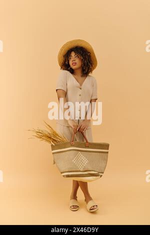 Eine schöne junge afroamerikanische Frau mit lockigem Haar, die elegant einen Korb hält, mit Strohhut und Sommerkleid verziert. Stockfoto