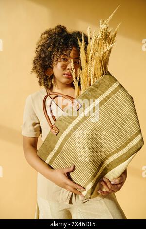 Eine schöne junge afroamerikanische Frau mit lockigen Haaren hält einen Korb Weizen in den Händen und verkörpert Überfluss und Ernte. Stockfoto